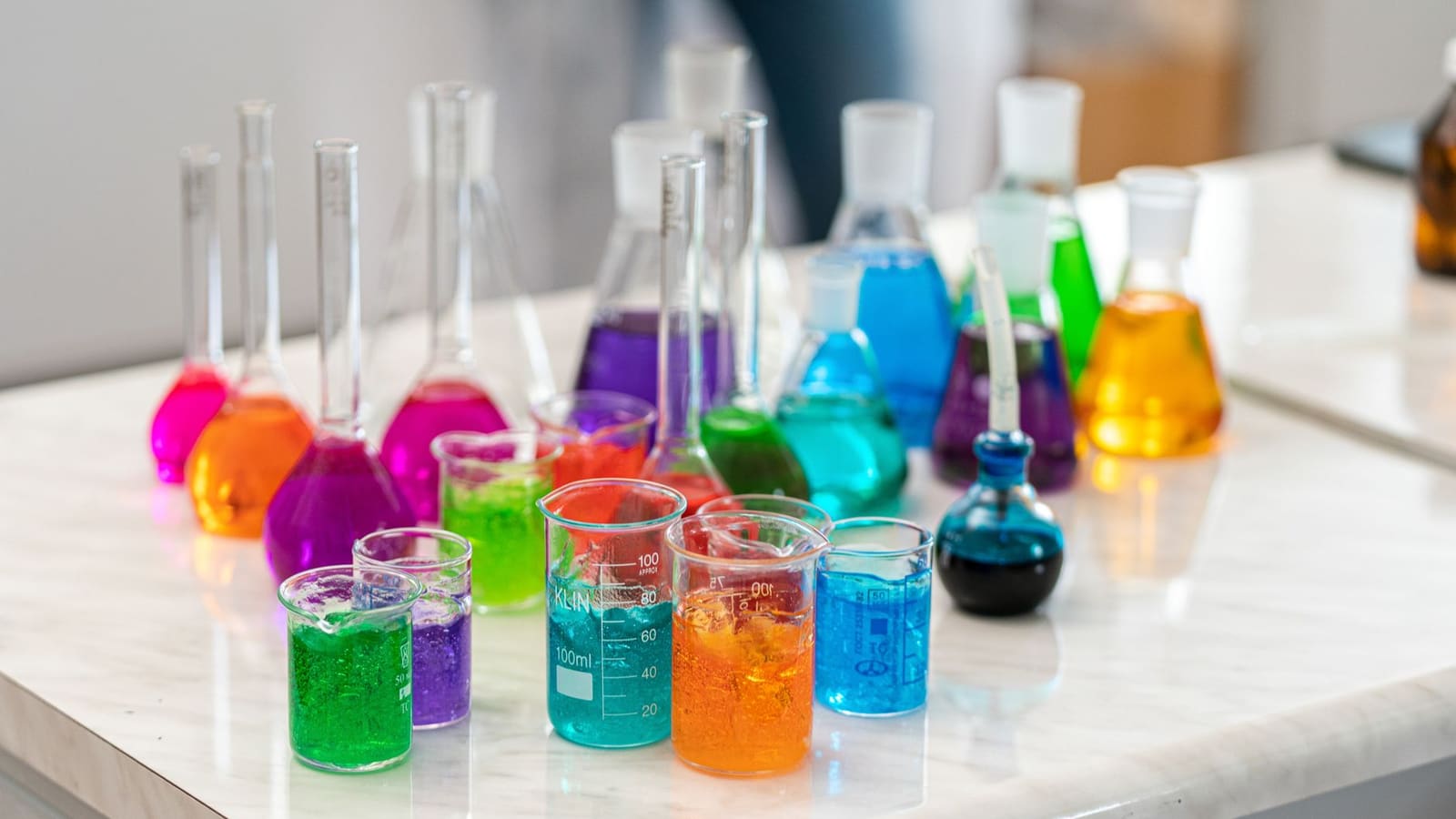 Beakers and flasks of bright pink, blue, purple and orange liquid lined up on a kitchen table
