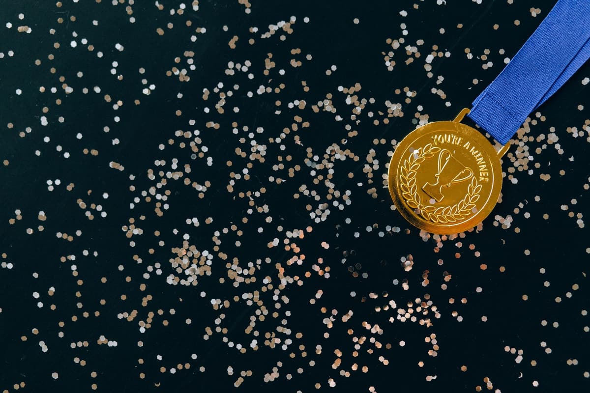 Close-up of a gold medal with blue ribbon and confetti on a black surface, symbolizing victory
