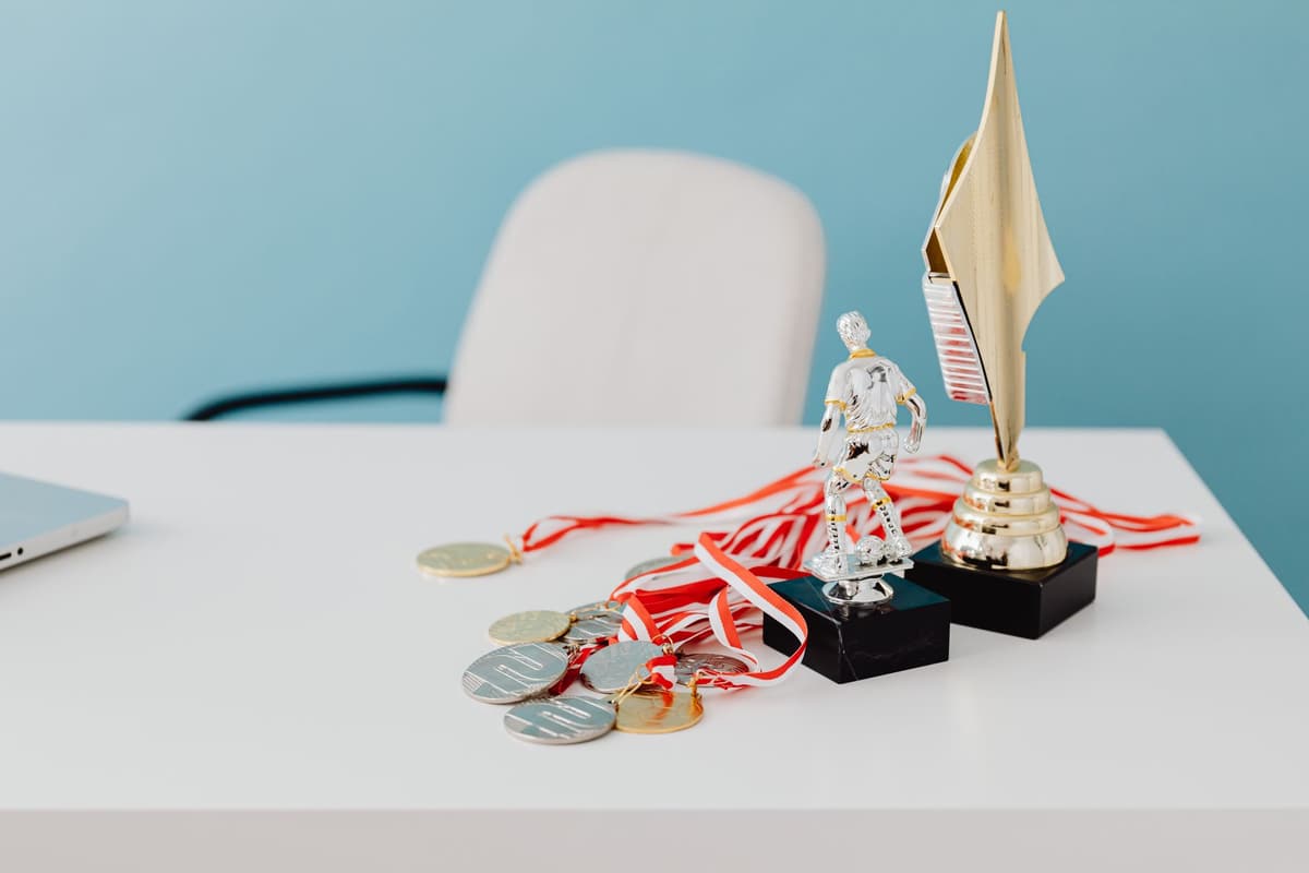 A collection of trophies and medals displayed on a white desk, symbolizing success and victory