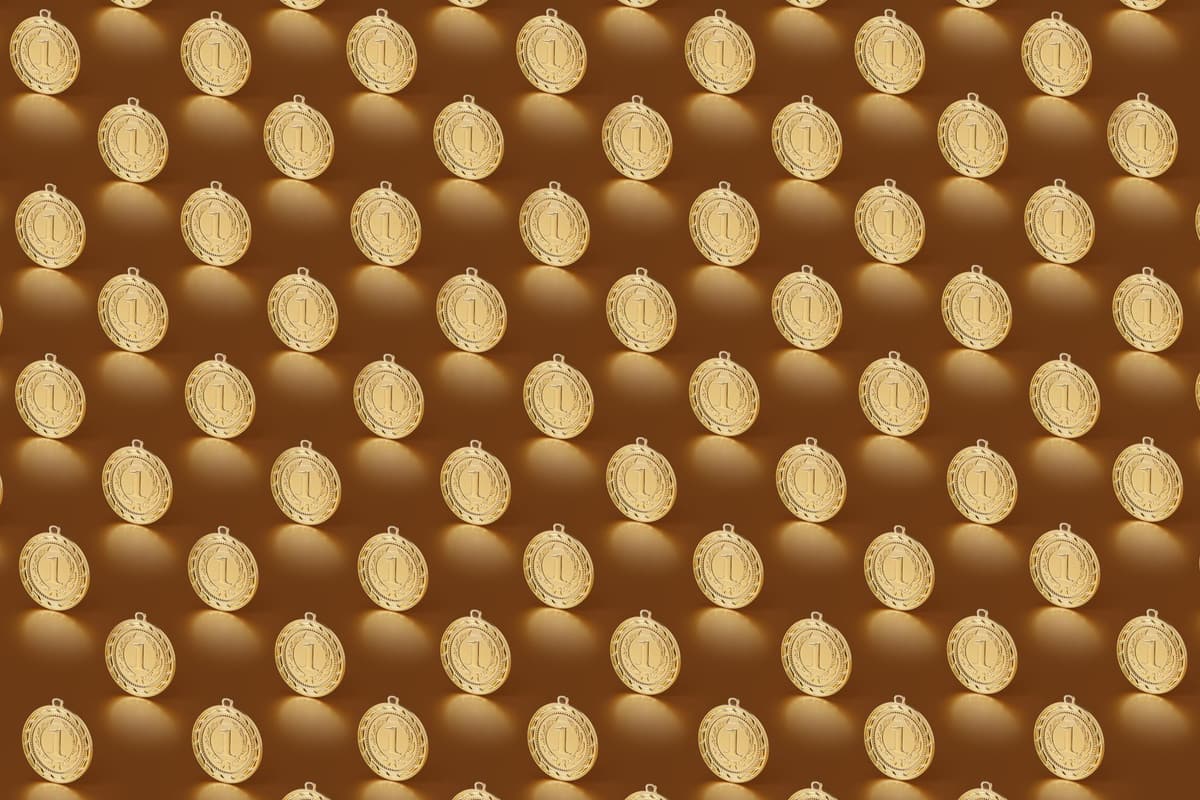 Multiple gold medals arranged in a repeating pattern on a brown backdrop