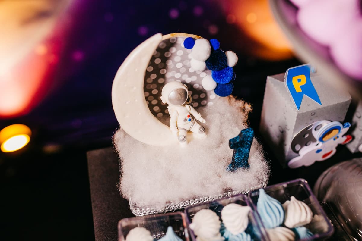 A close-up of a space-themed cake decoration with an astronaut figurine and the number one in a cosmic setting