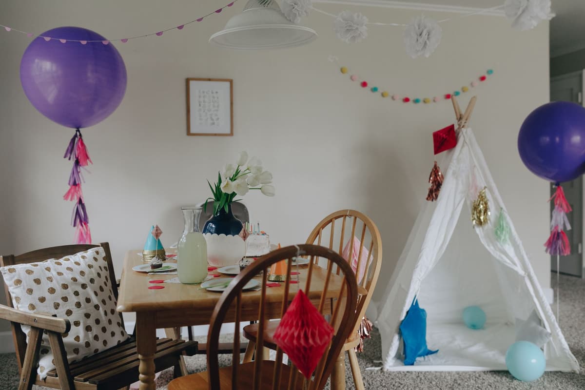 Charming indoor birthday party decor featuring balloons, a teepee tent, and a decorated dining table in a cozy apartment