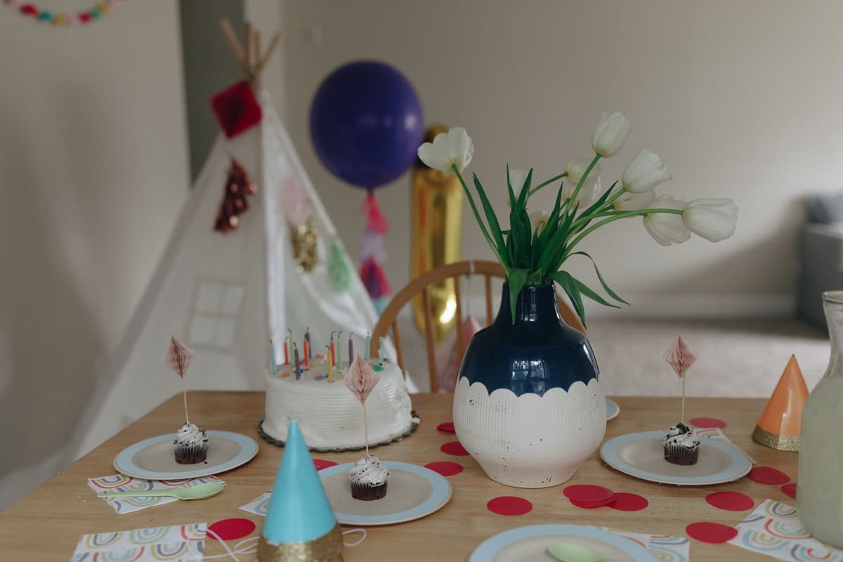 Festive indoor birthday setup with cake, cupcakes, flowers, and party decor