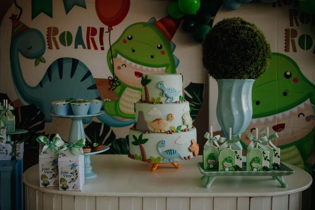 Colorful dinosaur-themed birthday cake and table setup with decorations for a children's party