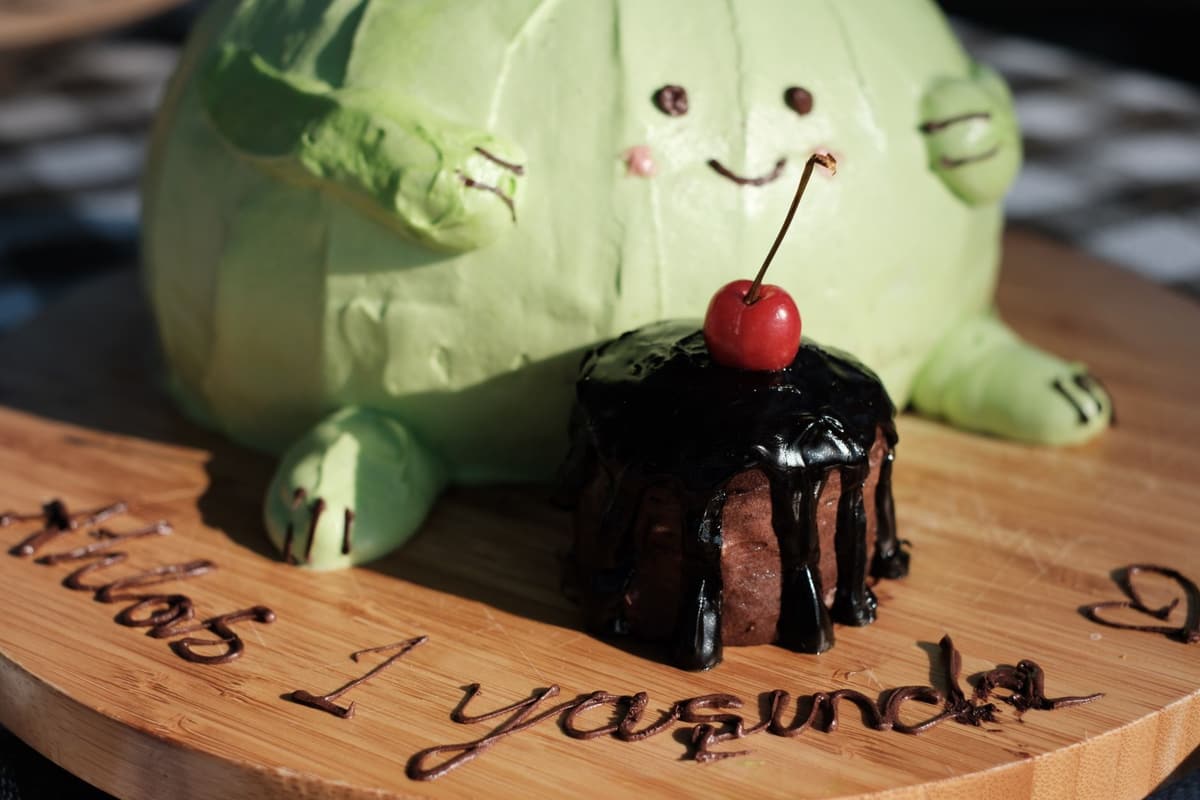 Charming green dinosaur cake with a chocolate dessert, topped with a cherry. Perfect for a child's birthday celebration