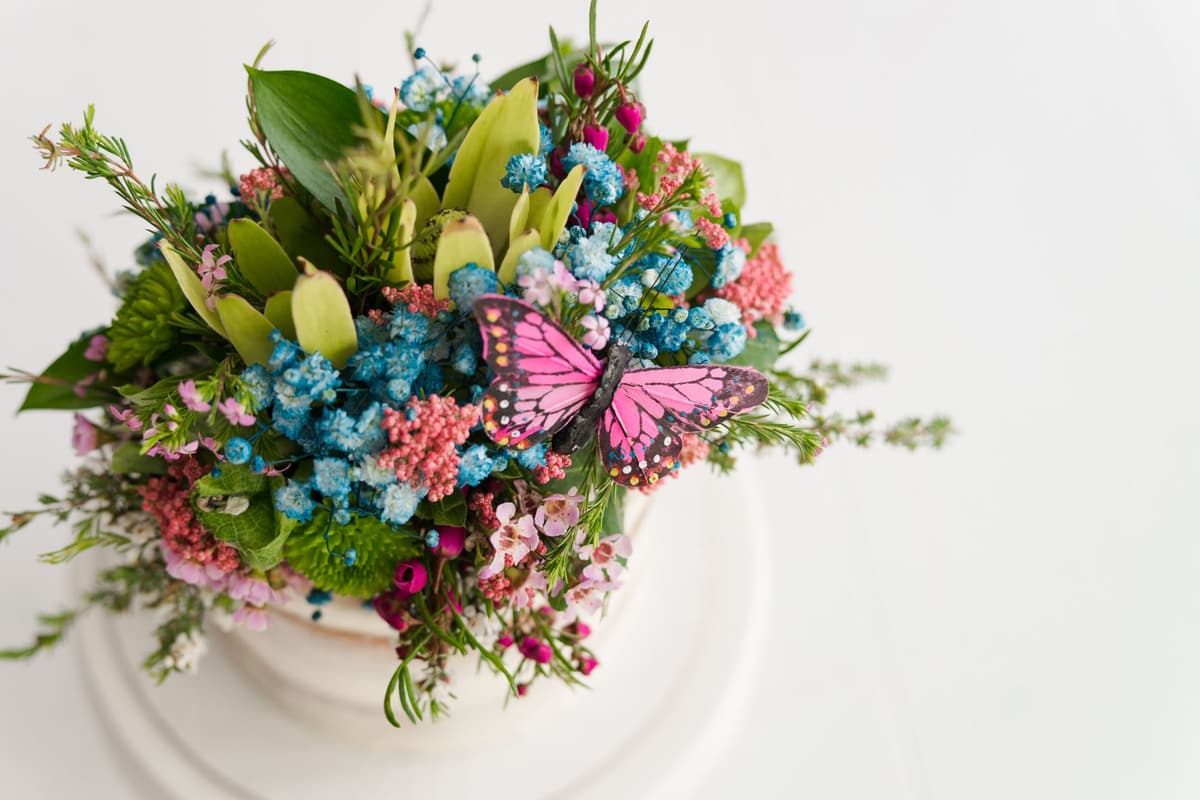 Vibrant flower arrangement on cake with pink butterfly topper, perfect for celebrations
