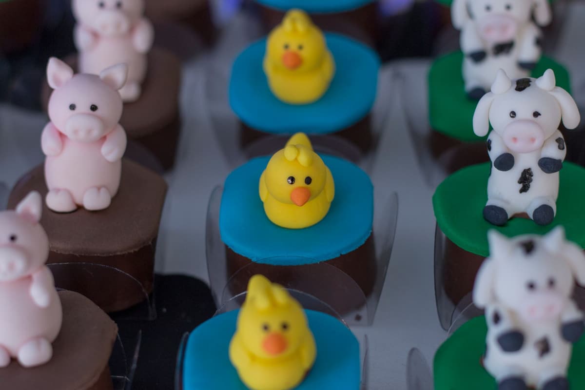 Whimsical cupcakes topped with fondant animals including pigs, ducks, and cows, perfect for dessert lovers