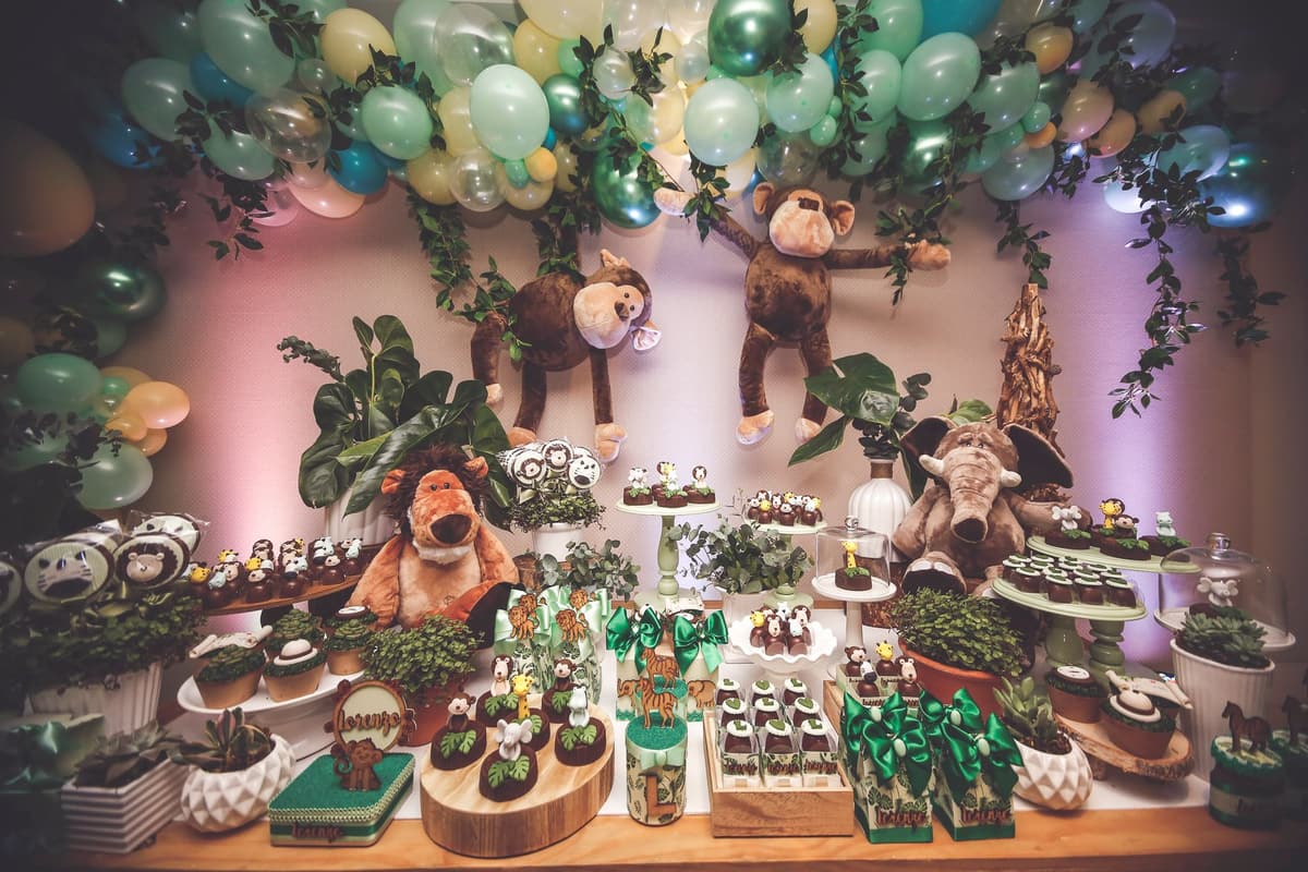 Whimsical jungle-themed dessert table for a birthday, featuring plush animals and green decorations