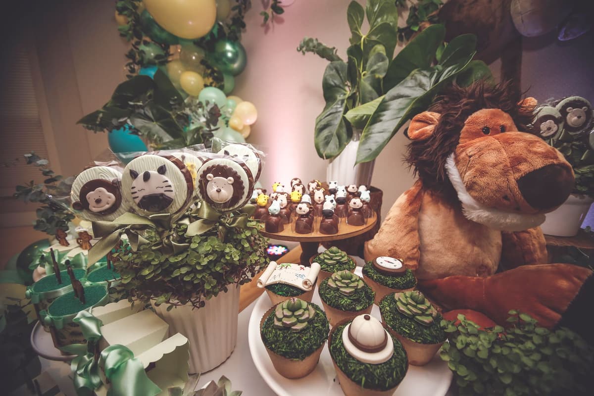 A vibrant jungle themed dessert table featuring animal cupcakes and plush toys