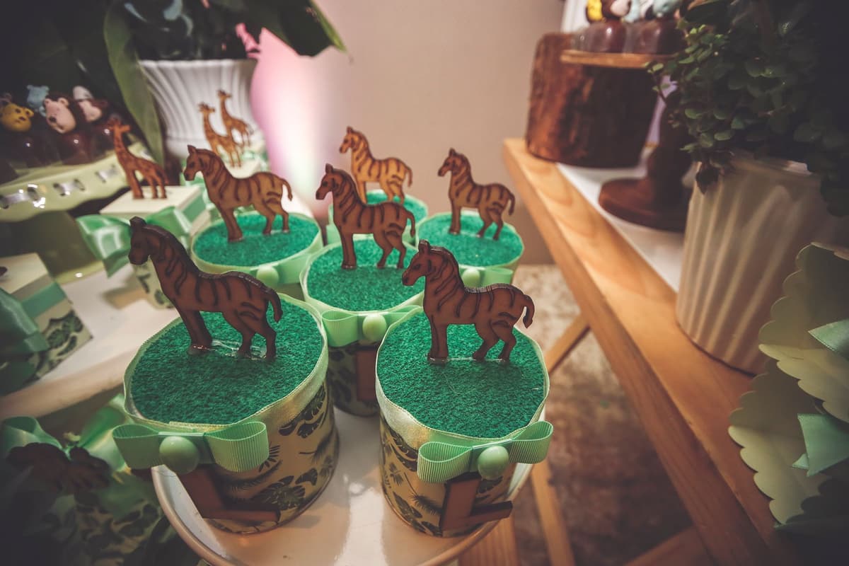 Colorful animal-themed cupcakes decorated with toy horses on a dessert table