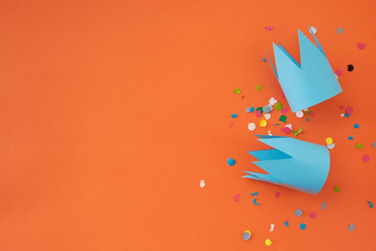 Vibrant paper crowns with colorful confetti on an orange surface, ideal for festive themes