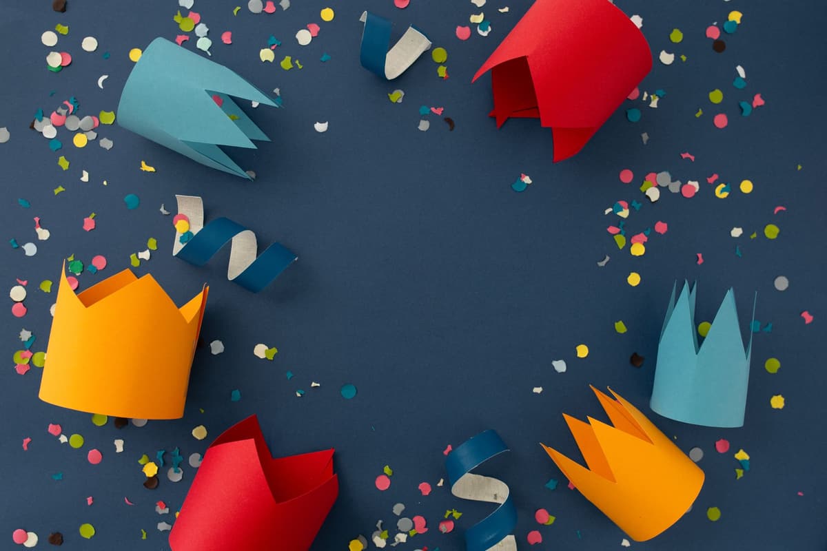 Vibrant paper crowns and confetti on a blue backdrop, perfect for festive celebrations