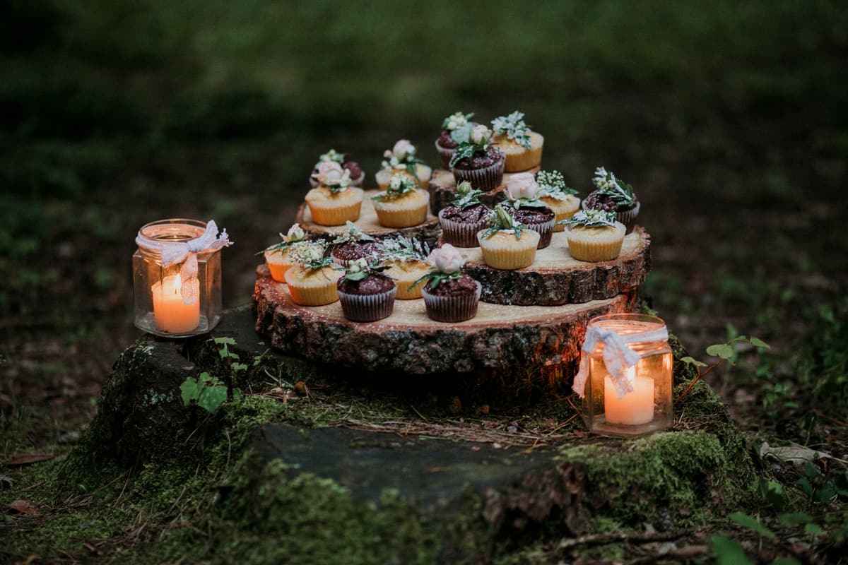 A charming display of cupcakes on a mossy tree stump with candles, creating a rustic outdoor ambiance