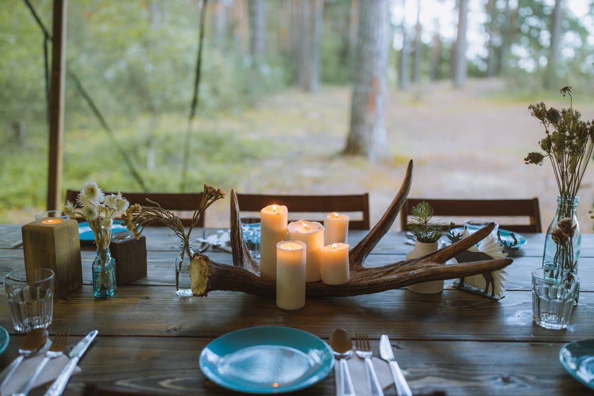 A rustic dining table set outdoors with candles, floral arrangements, and wooden decor