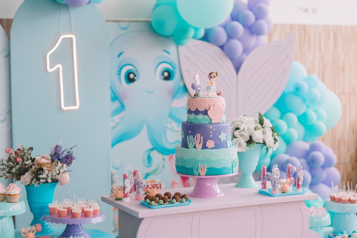 Vibrant mermaid-themed first birthday party decoration with cake, balloons, and sweets