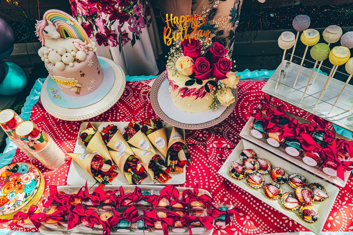Vibrant birthday party table setup with unicorn and rose cakes, desserts, and decorations